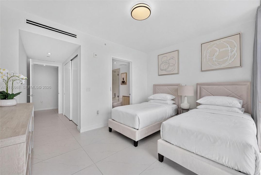Neutral-toned tile flooring, recessed linear climate control ducting, dual sliding-door closets, and a flush-mount drum ceiling light fixture