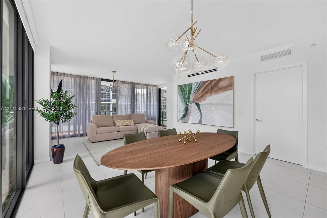 Open-concept interior featuring large-format tile flooring, floor-to-ceiling glass wall, and a multi-globe branching chandelier