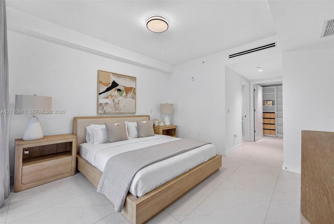 Large-format tile flooring, recessed linear climate control integration, and a walk-in closet featuring custom built-in shelving and drawer units