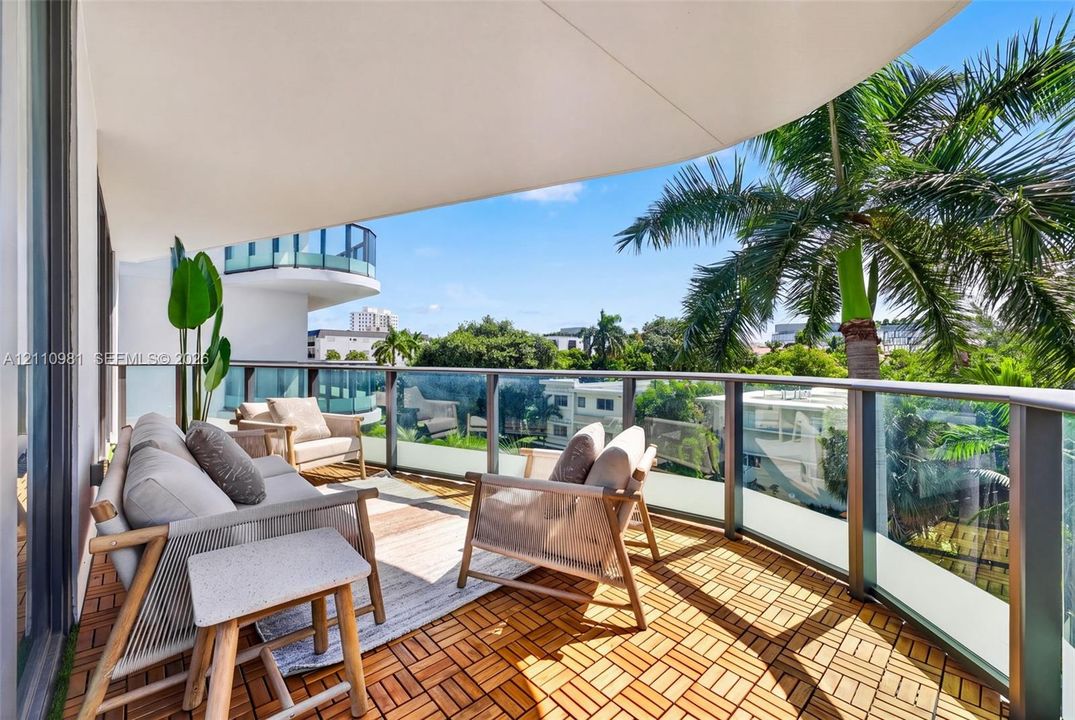 Covered balcony featuring wood-finish deck tiling, glass-paneled railings, and a curved architectural overhang