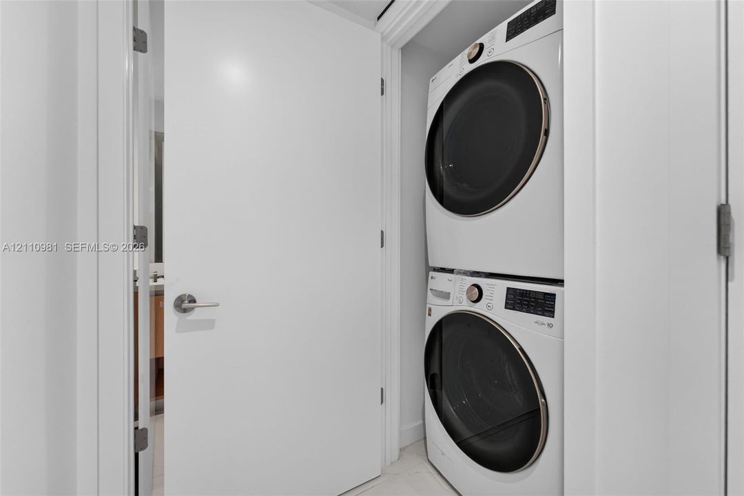 Stacked laundry unit featuring a high-efficiency front-load washer and dryer with circular glass doors and integrated digital control panels