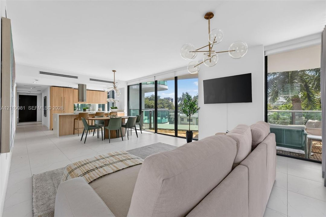 Open-concept interior featuring light-toned flooring, floor-to-ceiling glass sliding doors, minimalist cabinetry, stainless steel range hood, and multi-arm geometric pendant lighting