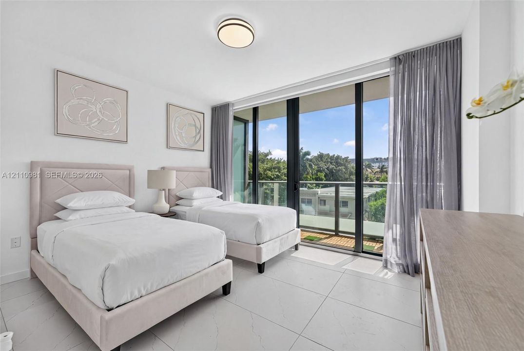 Floor-to-ceiling glass sliding doors, private balcony with metal railing, light-colored tile flooring, and flush-mount ceiling lighting
