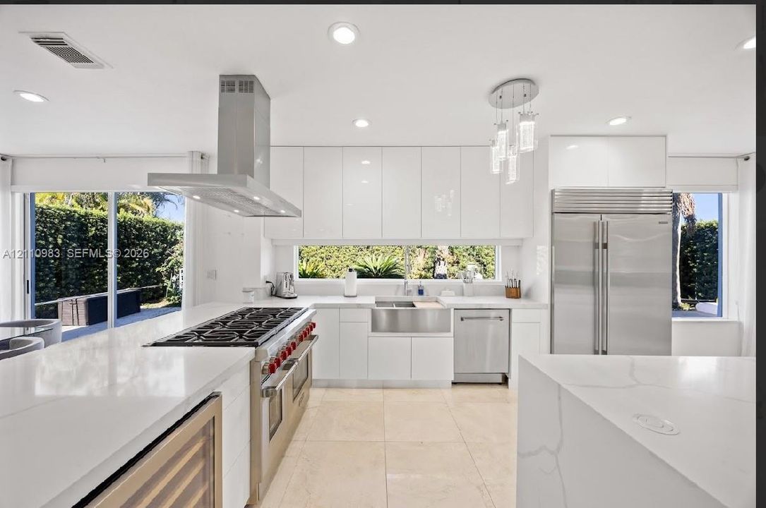 Modern kitchen featuring high-gloss white cabinetry, quartz countertops, stainless steel professional-grade range with a matching hood, apron-front sink, and integrated refrigeration
