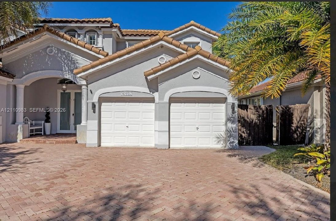 Stucco exterior with multi-gabled roofline, two-car garage, and paved brick driveway