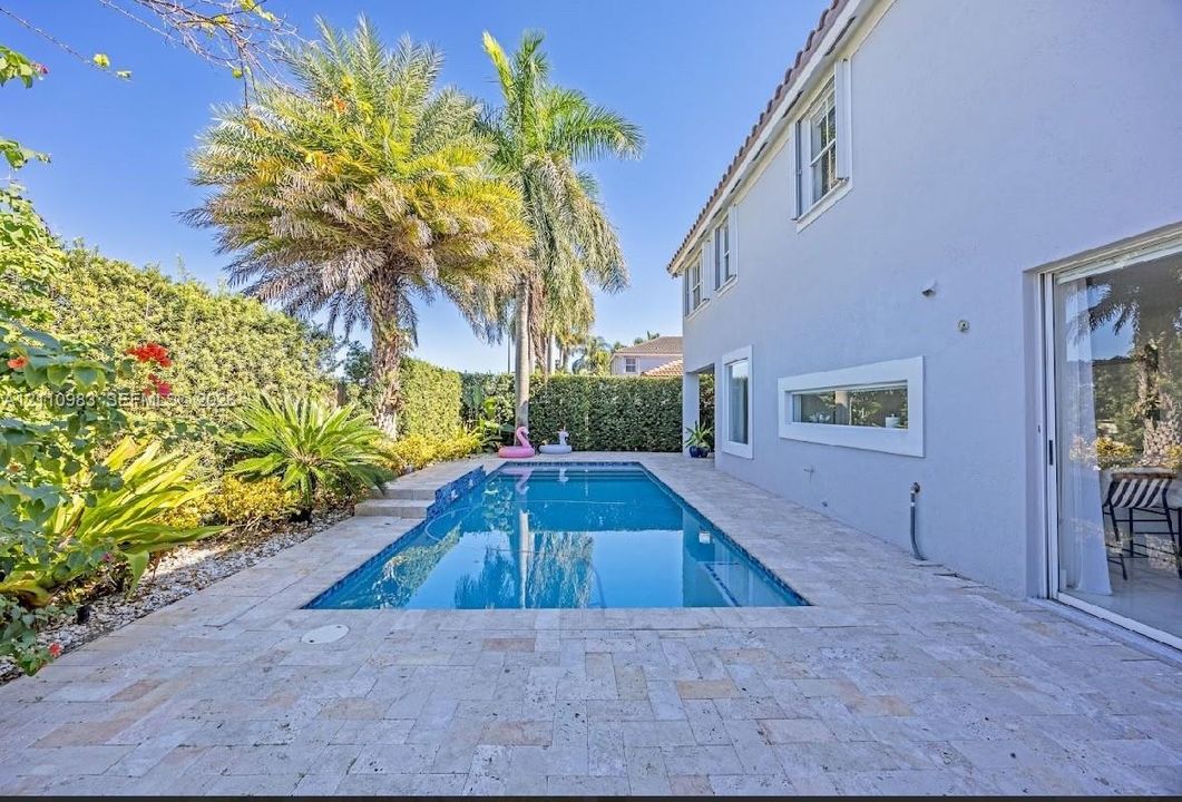 Rectangular in-ground pool with stone paver decking, lush perimeter landscaping, and sliding glass door access