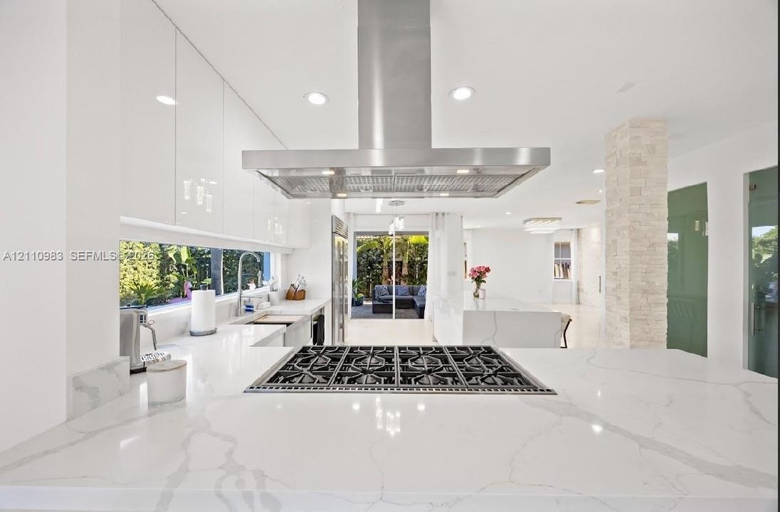 Modern kitchen featuring high-gloss cabinetry, a prominent stainless steel range hood, stone-finish countertops with veining, a built-in cooktop, and a stacked stone accent column