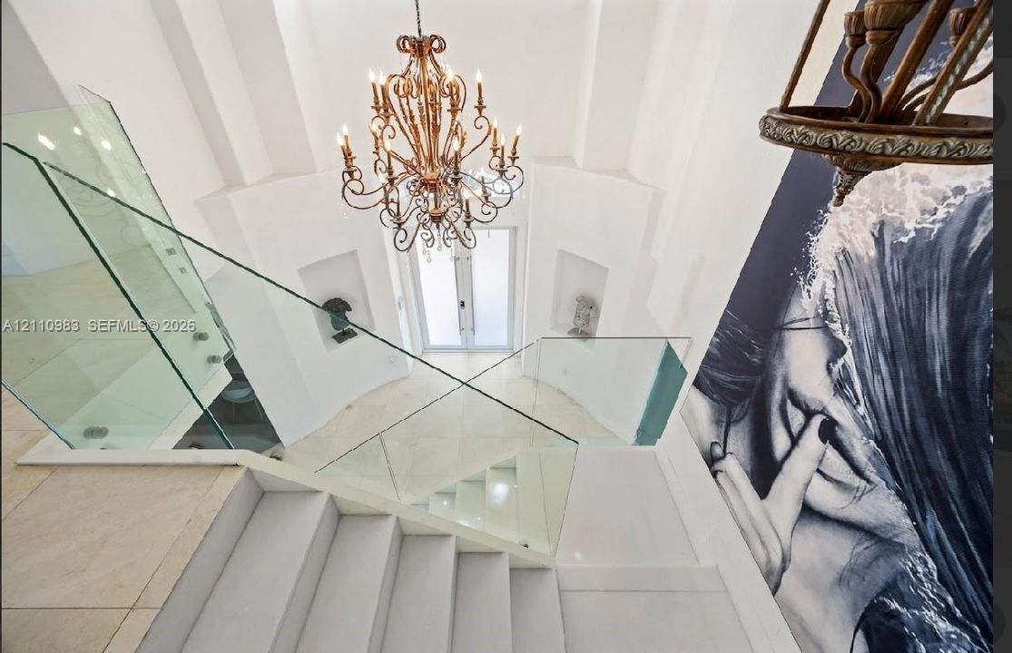 Foyer featuring a grand chandelier, glass panel railing, stone flooring, and arched wall niches