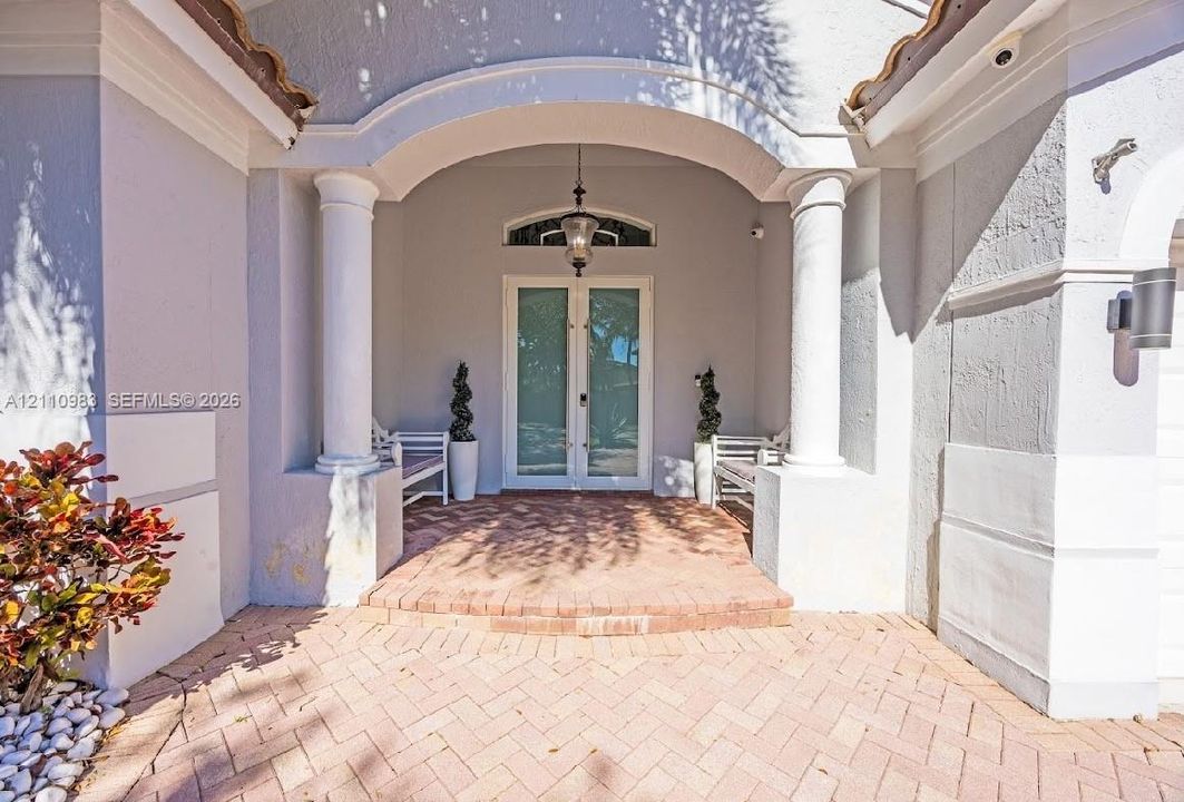 Covered entryway featuring a brick-paved porch, dual columns, a glass-paned double entry door with an arched transom window, and a hanging exterior lantern