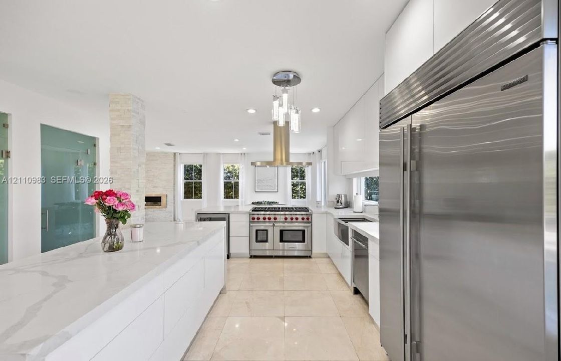 Kitchen featuring white flat-panel cabinetry, a stone-surfaced waterfall island, professional-grade stainless steel appliances, a stone-finished accent pillar, and polished stone flooring