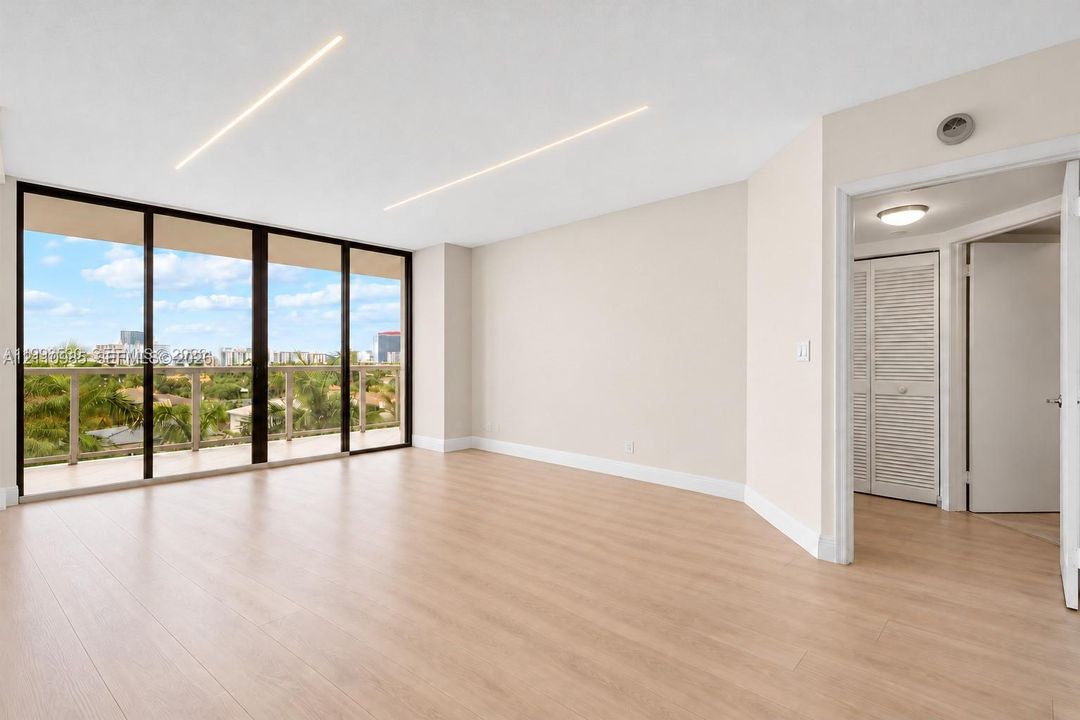 Virtually edited photo (digitally emptied/staged). Open-concept living space featuring floor-to-ceiling glass panel doors, wood-finish flooring, recessed linear lighting, and a closet with louvered doors.