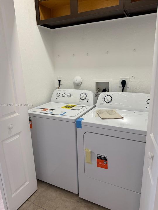 Laundry area featuring dark wood-finish upper cabinetry, ceramic tile flooring, and dedicated washer and dryer hookups