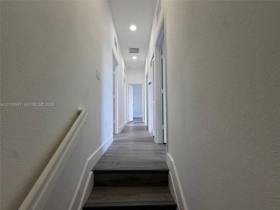 Hallway featuring wood-finish flooring, recessed lighting, and white walls with neutral trim
