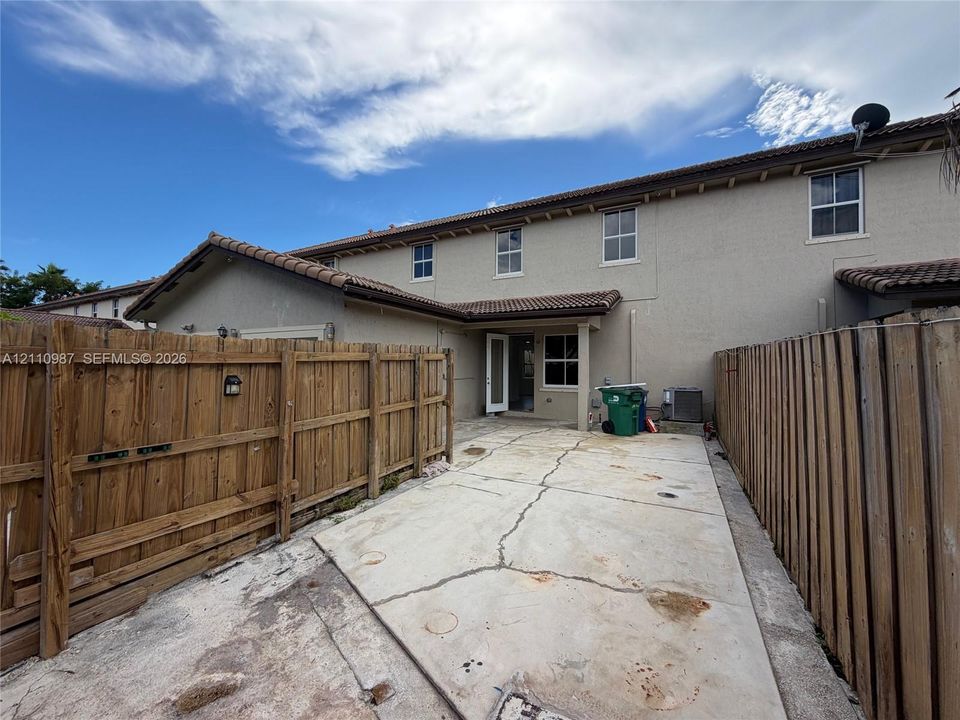 Exterior stucco facade with a tile roof and a private concrete patio enclosed by wood fencing