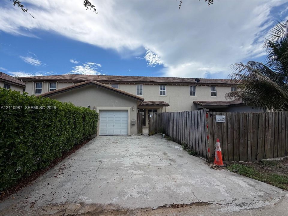 Two-story stucco exterior featuring a concrete tile roof, single-car garage, concrete driveway, and a wood privacy fence
