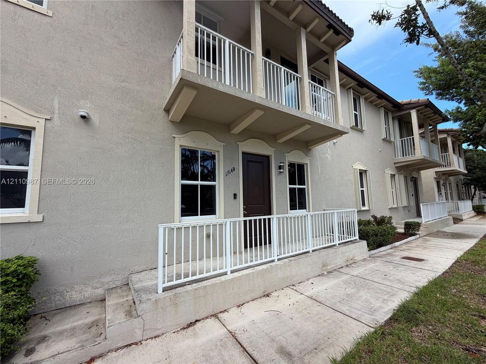 Stucco exterior featuring arched window trim, a private second-story balcony with metal railing, and a ground-level concrete entry porch enclosed by metal fencing