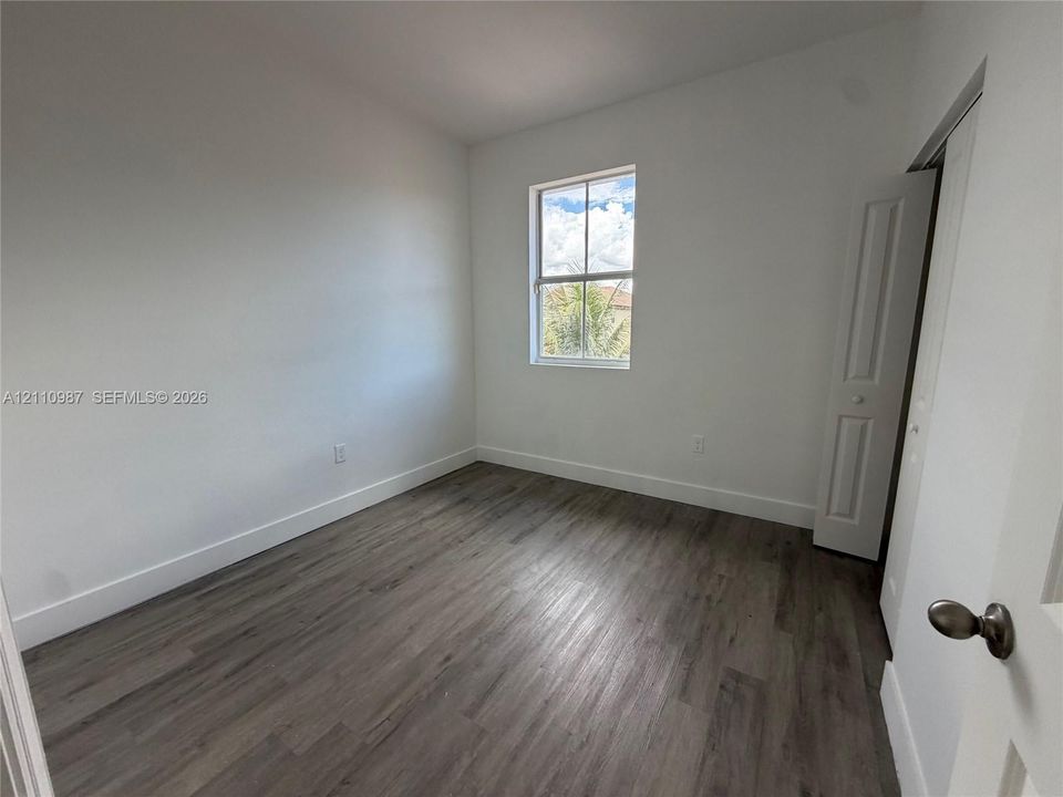 Interior space featuring wood-finish flooring, white walls, and a single-pane window with a folding closet door