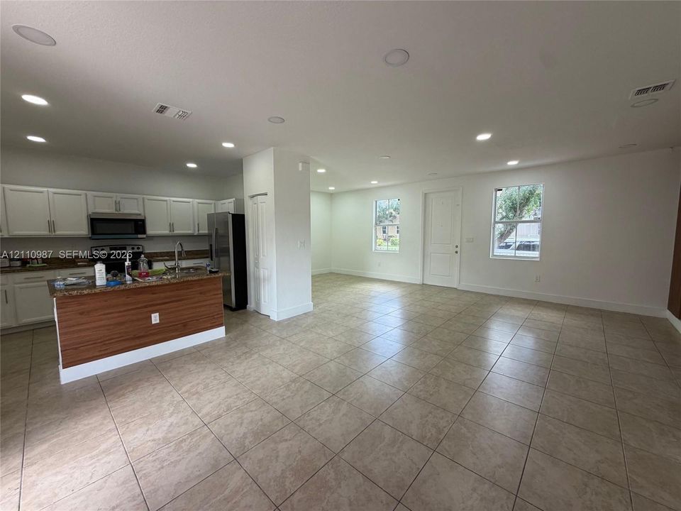 Kitchen featuring white shaker-style cabinetry, wood-finish center island, stone-patterned countertops, recessed lighting, and tile flooring