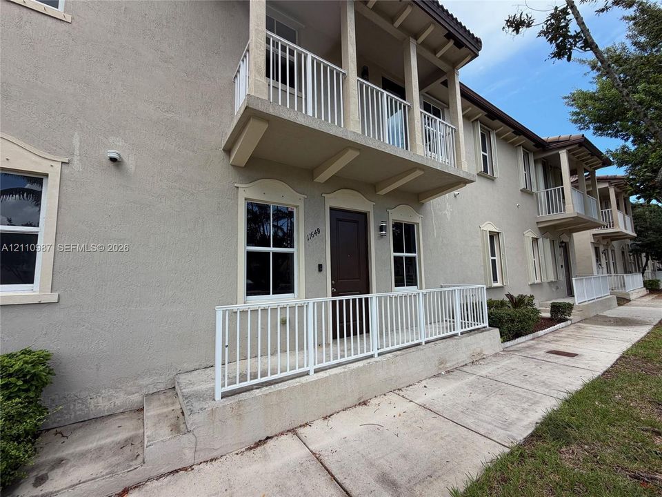 Stucco exterior featuring a second-story balcony with metal railing, raised concrete porch with matching metal railing, and decorative window molding