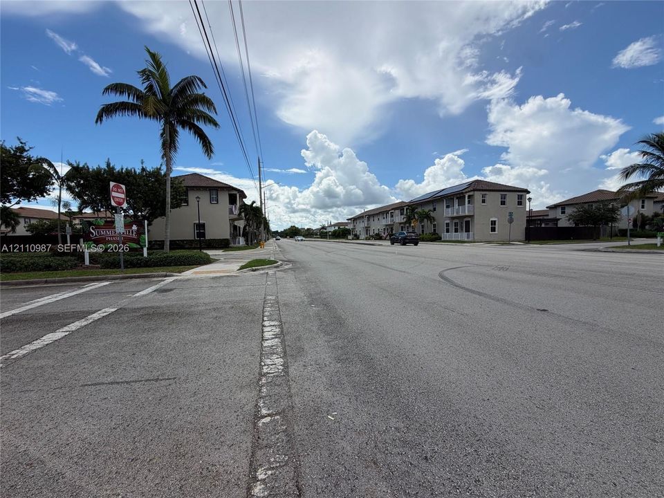 Multi-family residential exterior featuring stucco siding, hip roofs, covered balconies, and mature palm trees