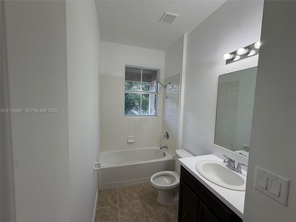 Bathroom featuring a single-sink vanity with a solid-surface countertop, dark wood-finish cabinetry, tile flooring, and a shower-tub combination with a tiled surround