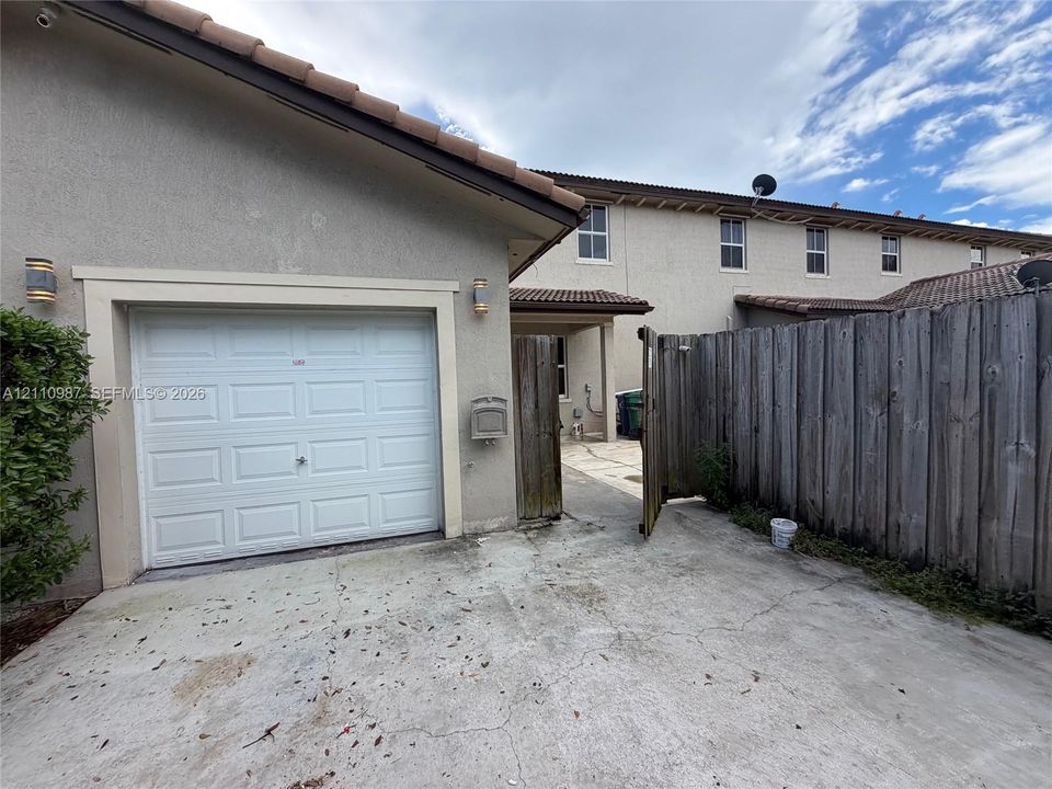 Exterior featuring a concrete driveway, single-car garage with white paneled door, stucco siding, tiled roof, and wood privacy fencing