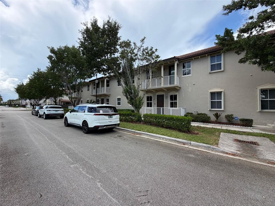 Two-story stucco exterior featuring covered balconies, recessed entryways, tile roof, and manicured shrubbery