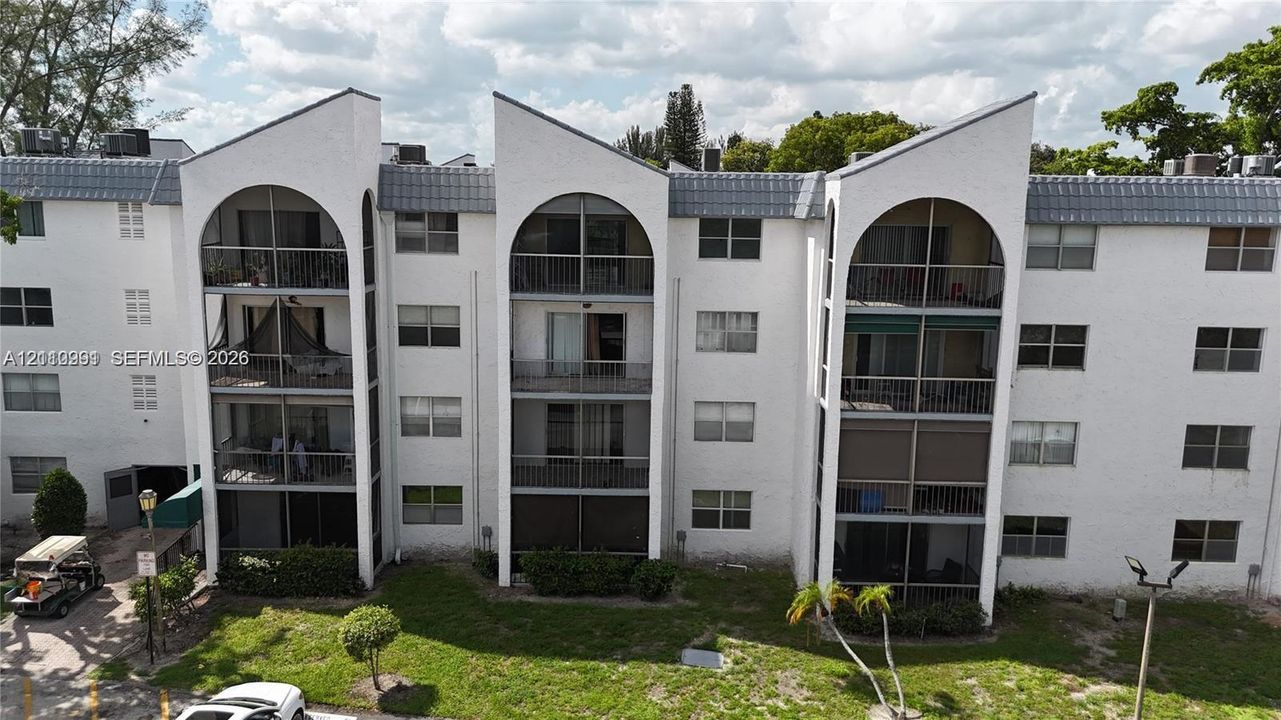 Multi-story building exterior featuring distinctive arched architectural elements, recessed screened balconies, and a light-colored stucco finish