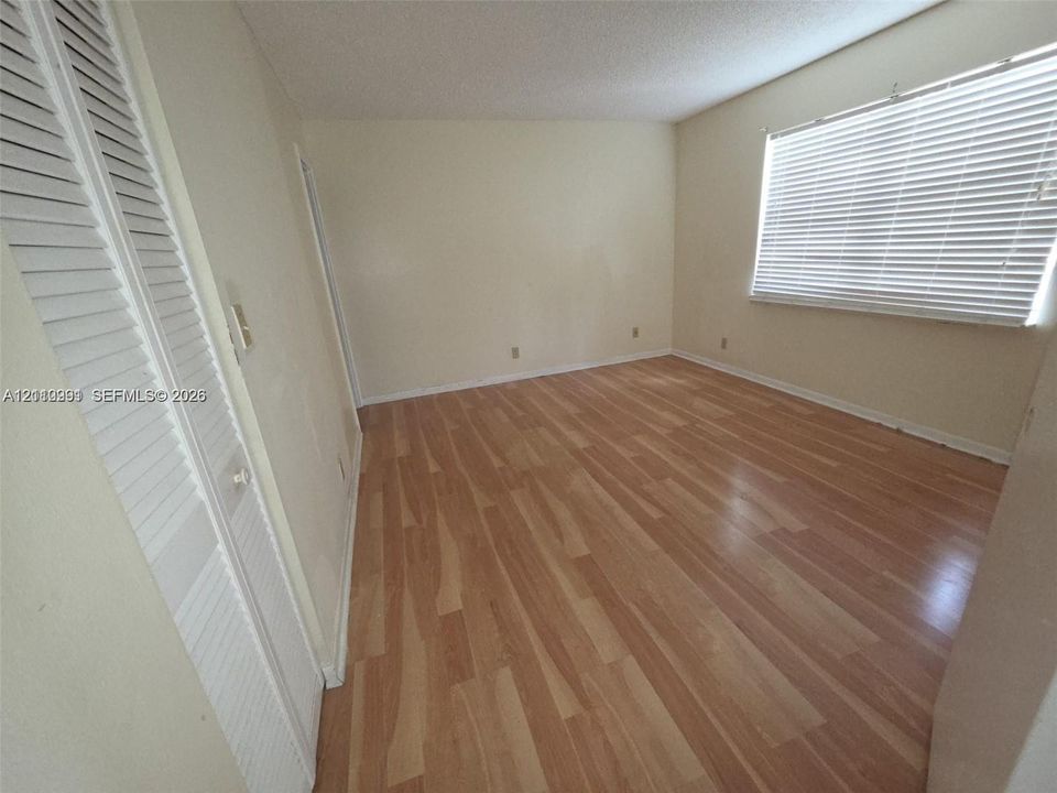 Room featuring wood-finish flooring, white louvered-style closet doors, and a window equipped with horizontal slat blinds