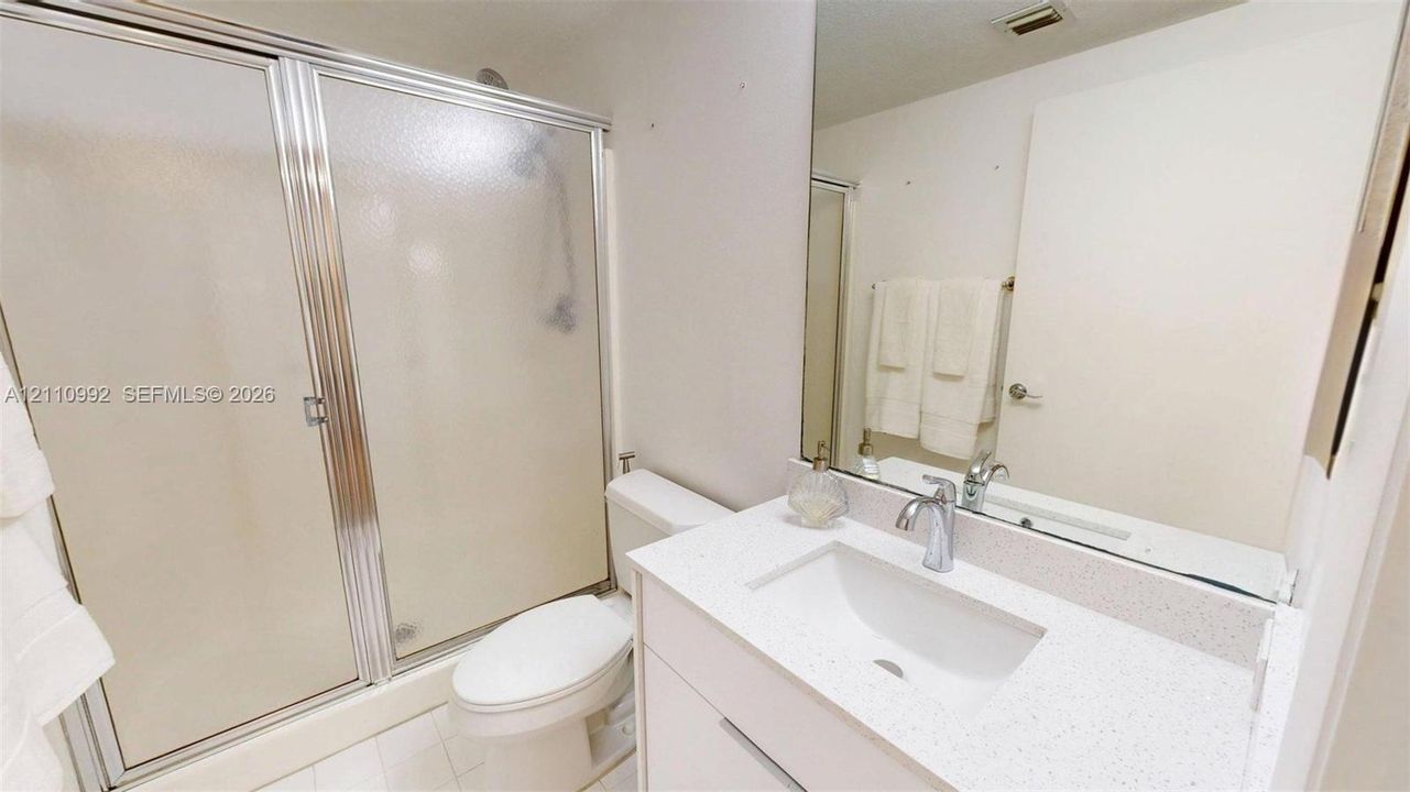 Bathroom featuring a vanity with a white composite countertop, integrated sink, chrome faucet, full-width mirror, and a glass-enclosed shower with a chrome frame