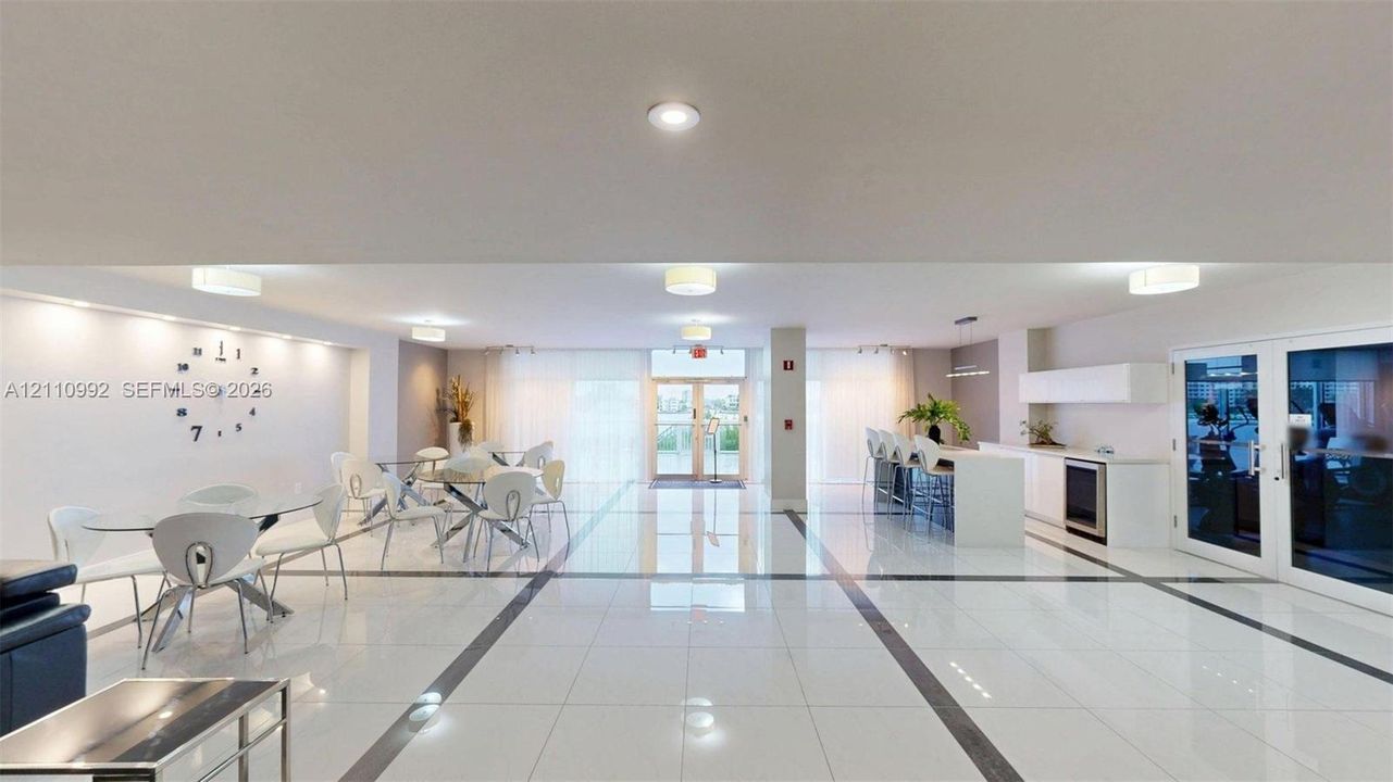 Expansive room featuring polished tile flooring with inlaid stone detailing, built-in wet bar with white cabinetry, recessed lighting, and double-glass entry doors