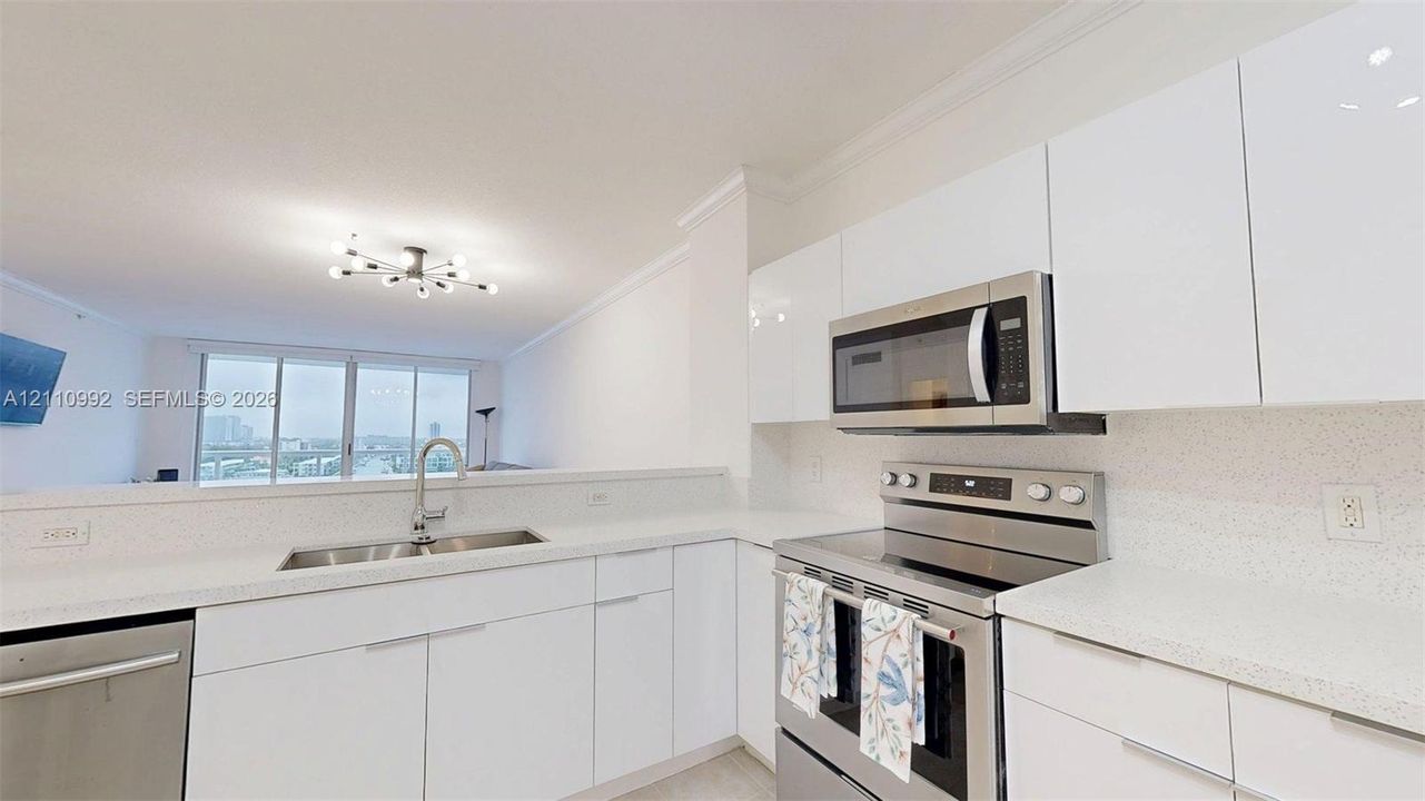 Kitchen featuring high-gloss white cabinetry, white stone-composite countertops, stainless steel appliances, and a polished chrome gooseneck faucet