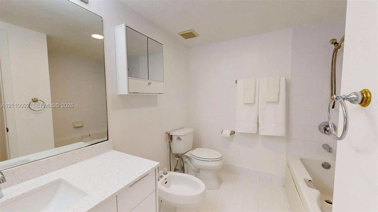 Bathroom featuring a stone-surface vanity countertop, an integrated rectangular sink, a mirrored medicine cabinet, a bidet, and a tile-surround shower and tub combination