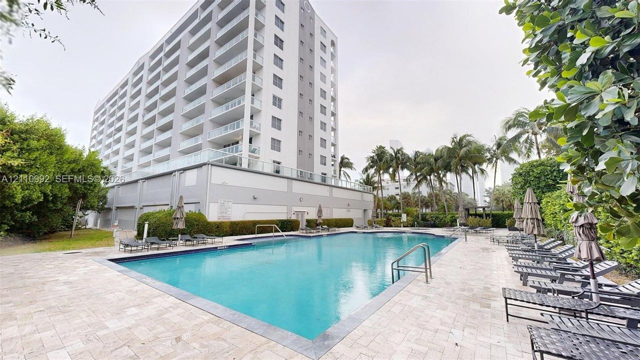 In-ground swimming pool featuring stone tile decking, metal handrails, and surrounding mature landscaping
