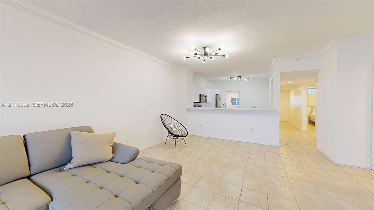 Neutral tile flooring, crown molding, multi-arm flush-mount lighting, and a breakfast bar counter