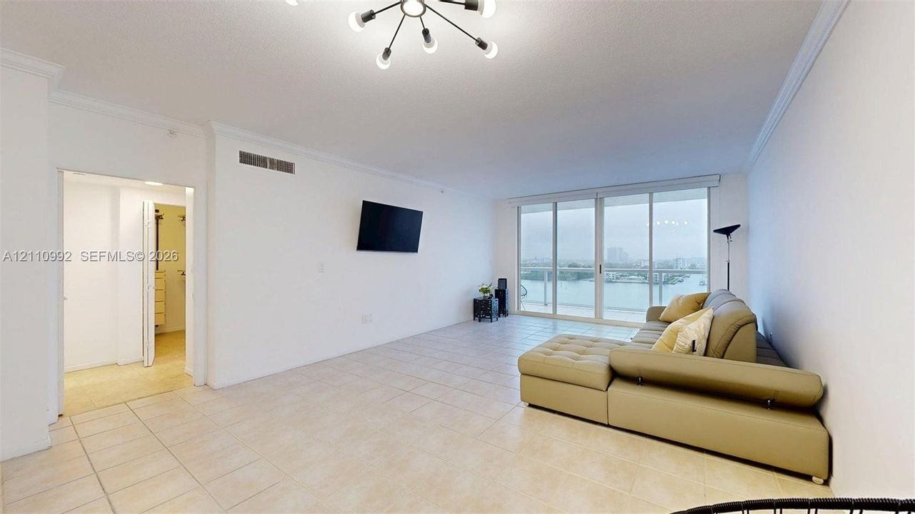 Open-concept living space featuring large-format tile flooring, a multi-arm modern ceiling light fixture, expansive floor-to-ceiling glass sliding doors, and a private balcony