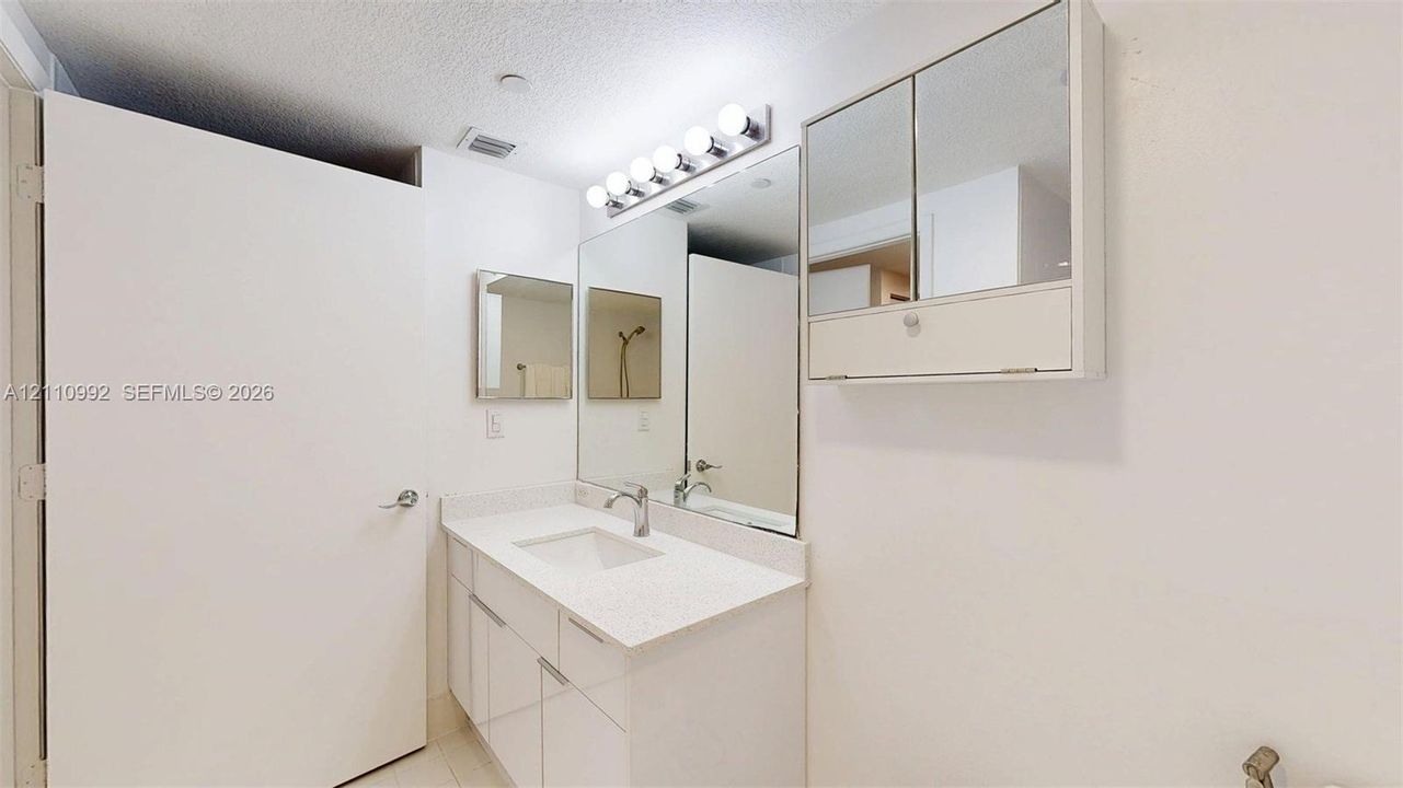 Bathroom vanity featuring a solid surface countertop, integrated rectangular sink, chrome fixtures, built-in medicine cabinet, and wall-mounted multi-bulb lighting