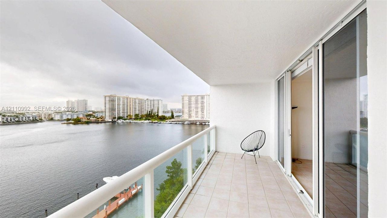 Private balcony featuring tile flooring and a glass-paneled railing, with sliding glass doors and expansive water frontage