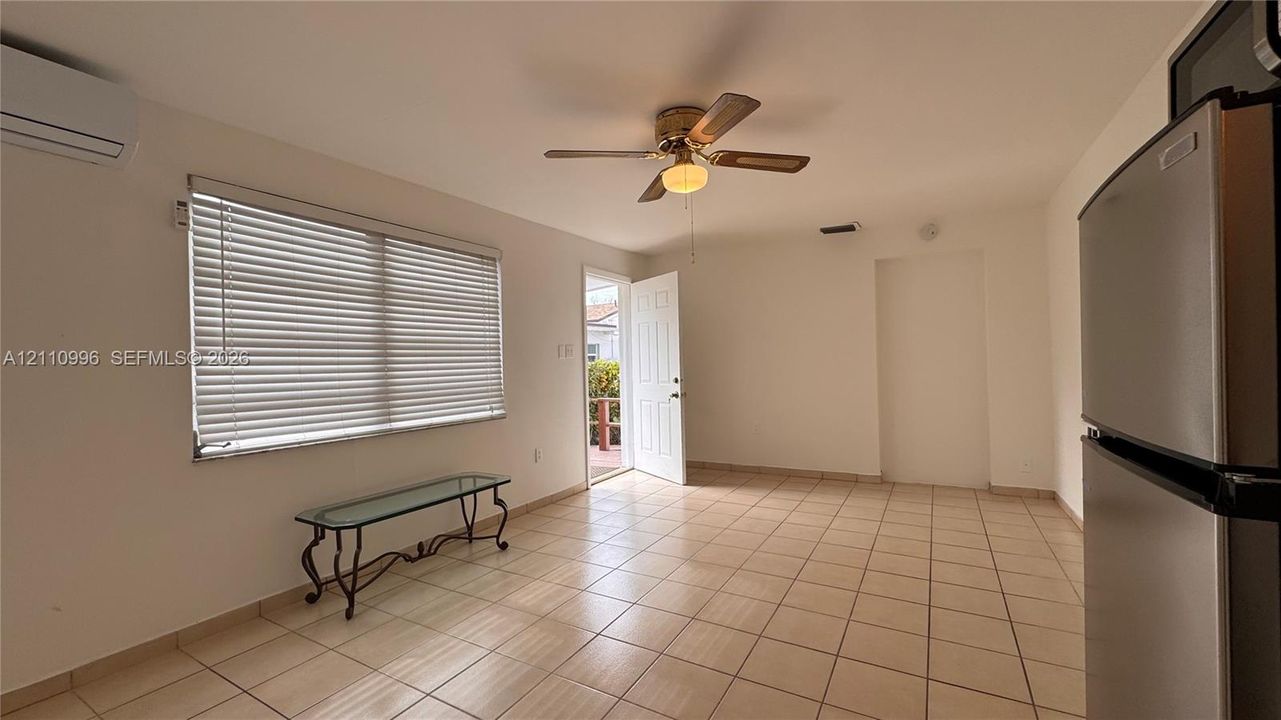 Interior space featuring tile flooring, a mounted ductless air conditioning unit, a multi-blade ceiling fan, and horizontal window blinds