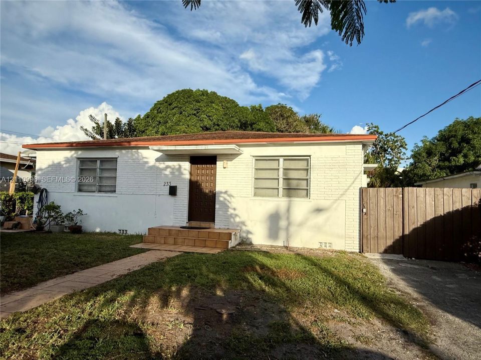Single-story residence featuring white painted brick exterior, horizontal sliding windows, a concrete walkway, and a full-height wooden privacy fence