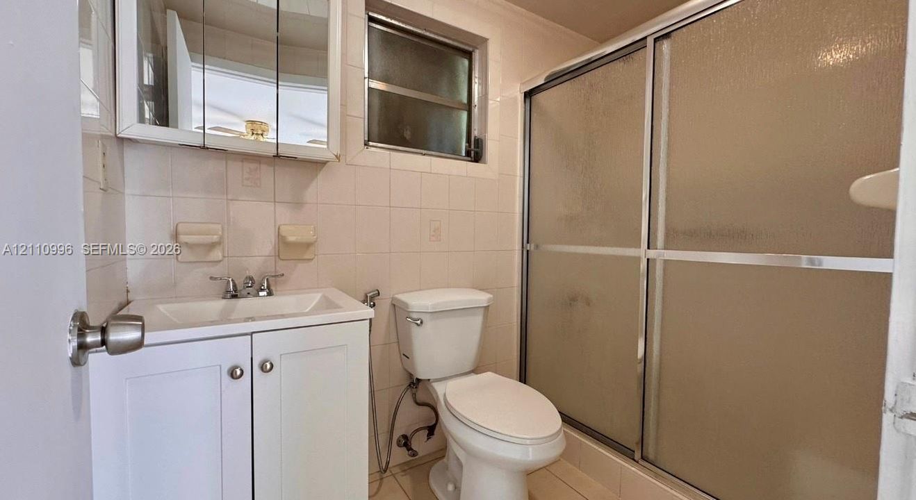 Bathroom featuring a white vanity cabinet, a wall-mounted medicine cabinet with a mirror, a ceramic tile shower enclosure with sliding glass doors, and white wall tile
