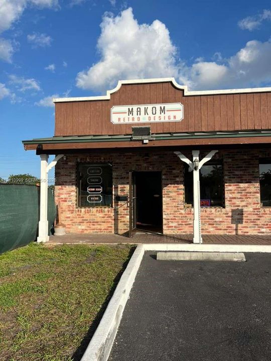 Commercial storefront featuring exposed brick masonry, wood-paneled upper façade, covered entryway, and asphalt parking area