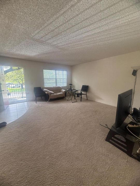 Neutral wall-to-wall carpeting, textured ceiling, ceramic tile flooring at the entry, and single-hung window with natural light