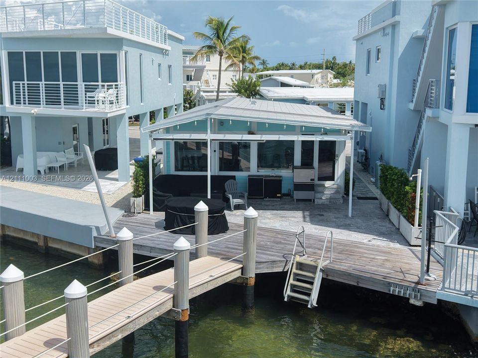 Waterfront exterior featuring a private wood dock, integrated swim ladder, covered patio with metal roofing, and multiple levels of balcony space