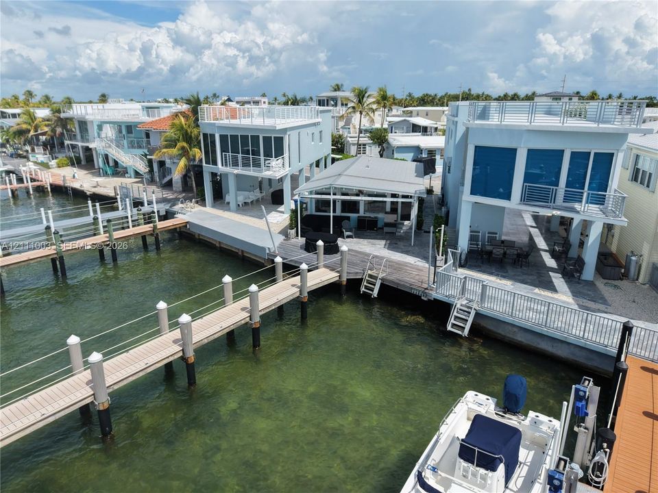 Waterfront multi-level structure featuring a private boat dock, rooftop deck with metal railings, covered ground-level patio, and sliding glass exterior doors