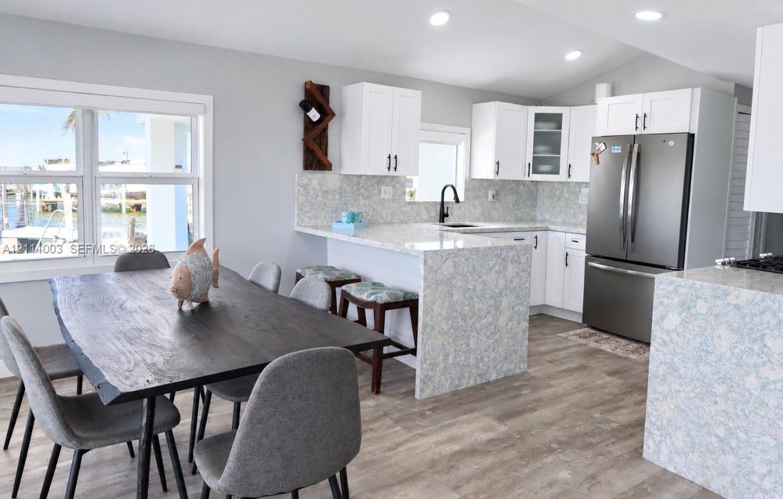 Kitchen featuring white shaker-style cabinetry, patterned stone-finish countertops with waterfall edge, wood-finish flooring, and recessed lighting
