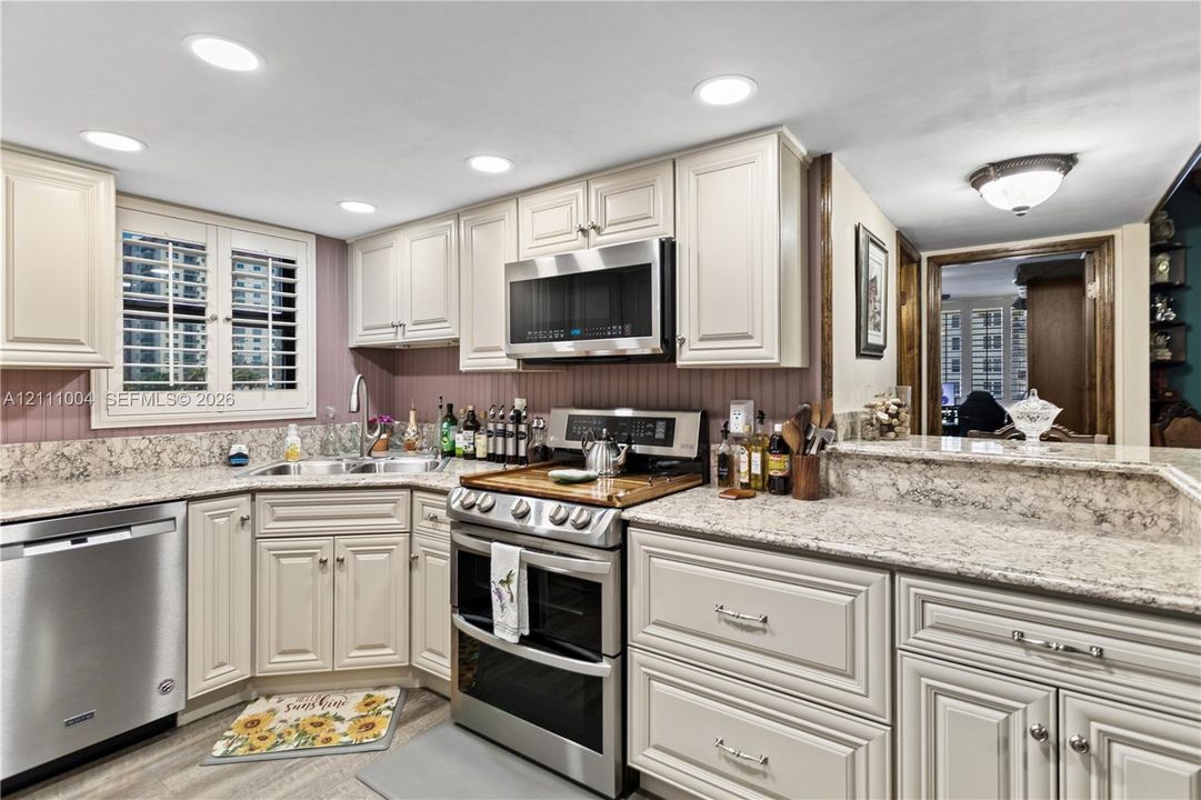 Kitchen featuring light-toned cabinetry, stone-finish countertops, stainless steel appliances, recessed lighting, and built-in shutter-style window coverings