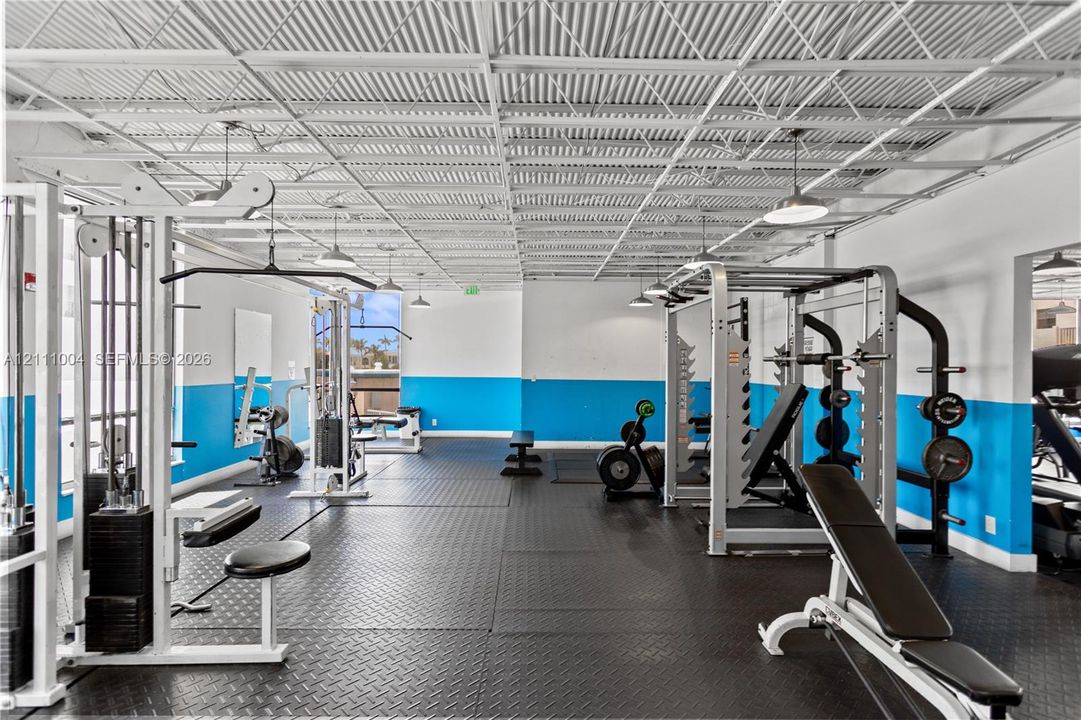 Fitness facility featuring industrial-style exposed metal ceiling grid, durable rubberized flooring, and recessed pendant lighting