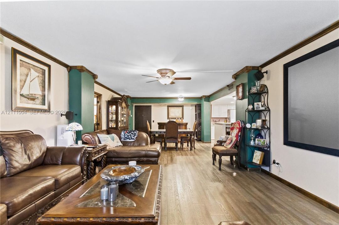Living area featuring wood-finish flooring, crown molding, dual-toned wall accents, and a central ceiling fan with an integrated light fixture