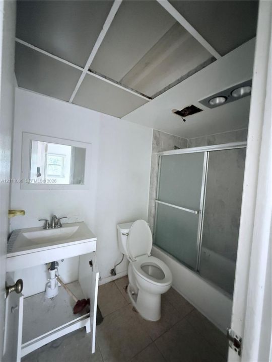Wall-mounted vanity with rectangular basin and chrome faucet, tile flooring, and shower enclosure with frosted sliding glass doors